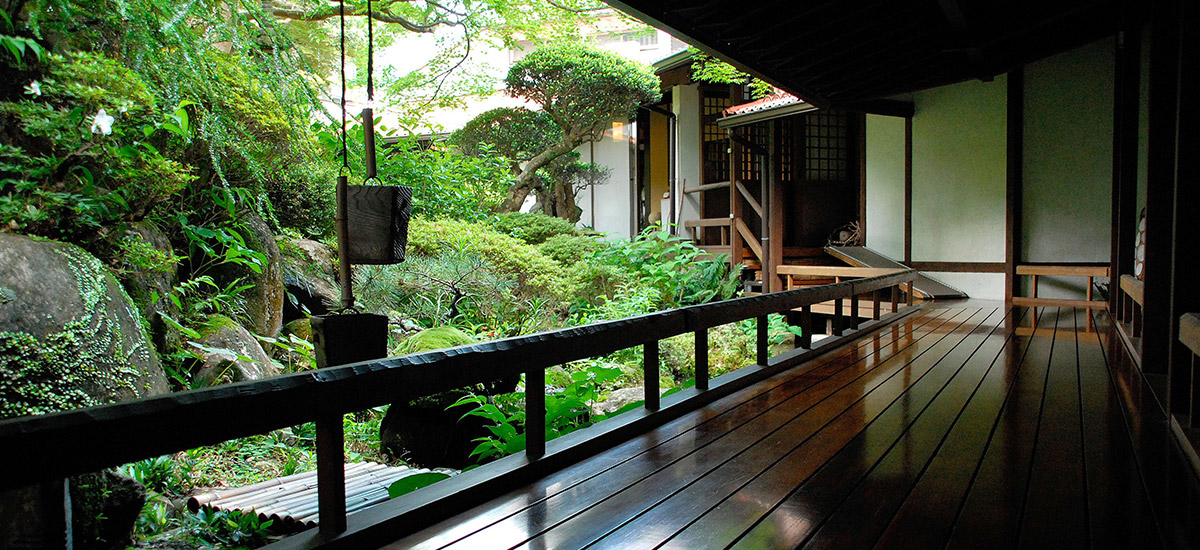 A covered timber walkway at Shirakabe opening onto moss, stone and the river garden