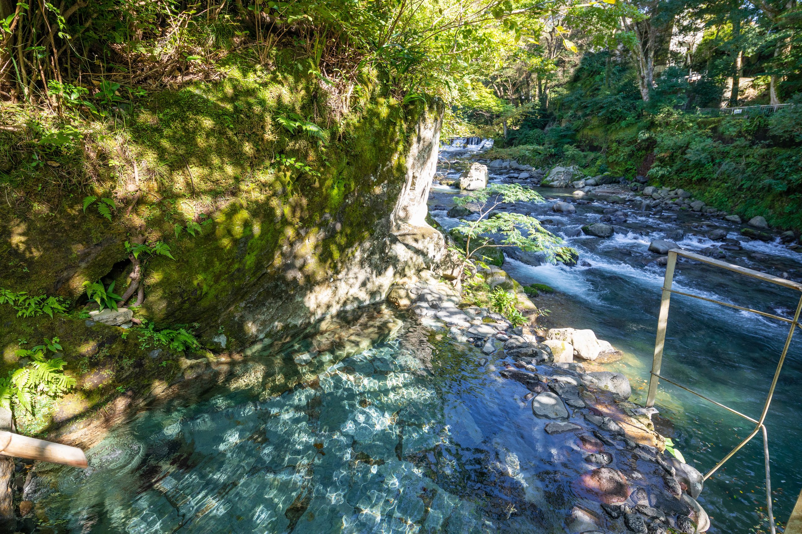 The riverside rock bath at Shirakabe: a clear spring-fed pool in the rock at the edge of the Kano River, moss and forest above